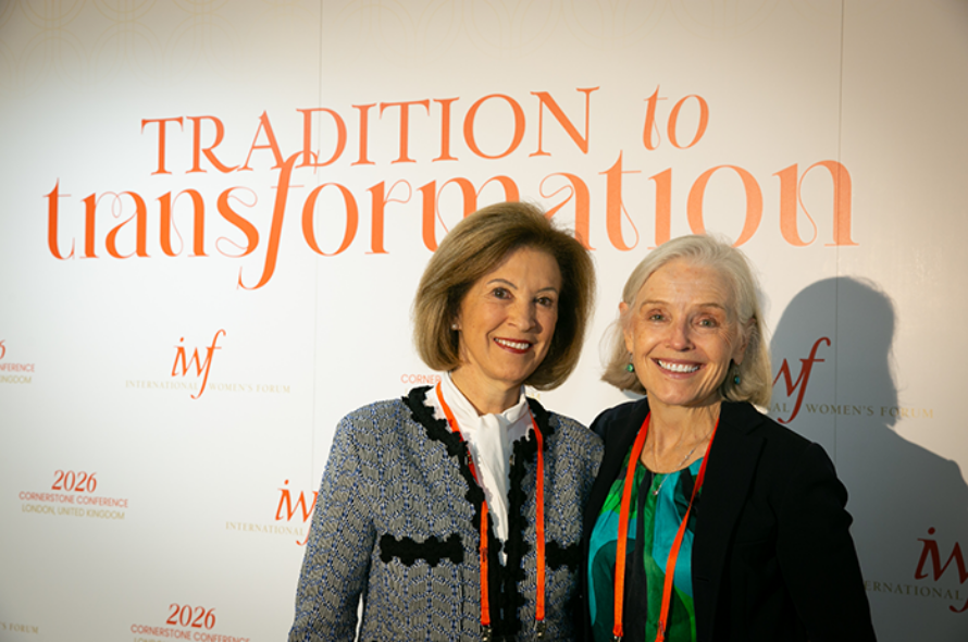 Two smiling women pose together at a conference backdrop that says 'Tradition to Transformation,' with event logos visible on the wall.